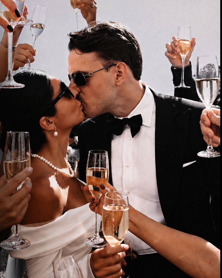 Newlyweds sharing a kiss surrounded by guests raising champagne glasses during a Fresh Chef wedding celebration.