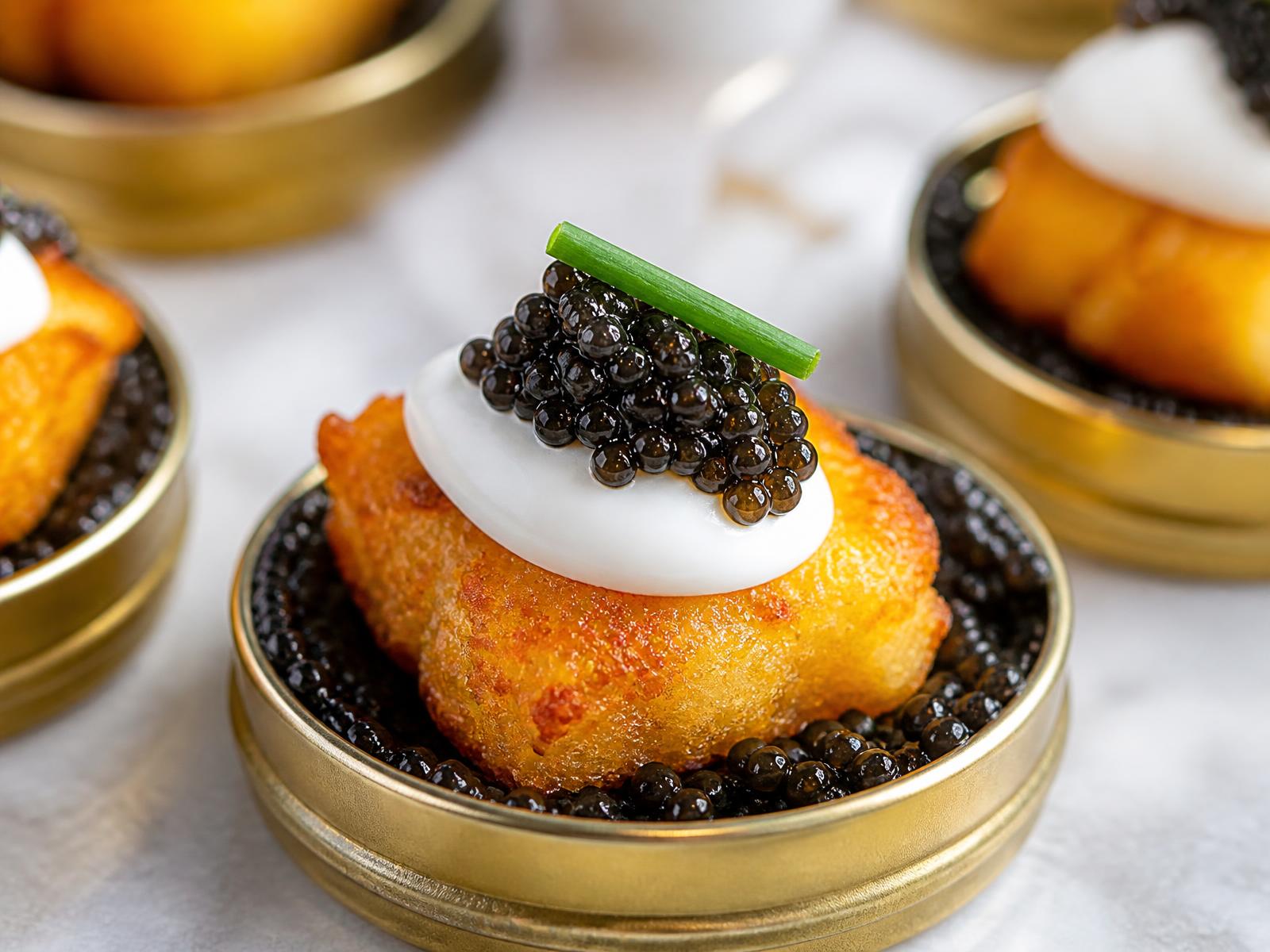 Golden crispy potato tots in individual caviar tins topped with crème fraîche and caviar